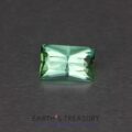 A rectangular, faceted 3.90-Carat Neon Blue-Green Indicolite Tourmaline is set against a dark, smooth background. The text "EARTH'S TREASURY Custom Gemstones & Fine Jewelry" is displayed below the gemstone.