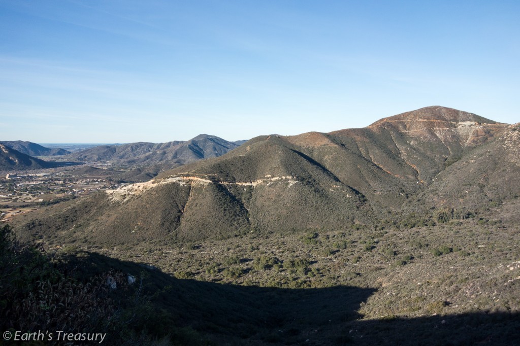 This photo shows Tourmaline Queen Mountain in Pala, California. The photo was taken from Chief Mountain, just to the east. You can clearly see evidence of mining activity on the mountain. On the south (left) end of the mountain, the Stewart Mine and associated roads scar the ridge. Near the more distant top of the peak (on the right), fainter road scars and an exposed mine dump mark the famous Tourmaline Queen Mine. Both of these mines would not be nearly as visible if a fire had not burned the mountain clear of most of the heavy brush in 2011.