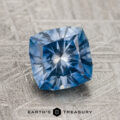 A 1.96-carat, medium blue Montana Sapphire (Heated) with intricate facets rests on a textured gray surface. "Earth's Treasury" appears at the bottom of the image.