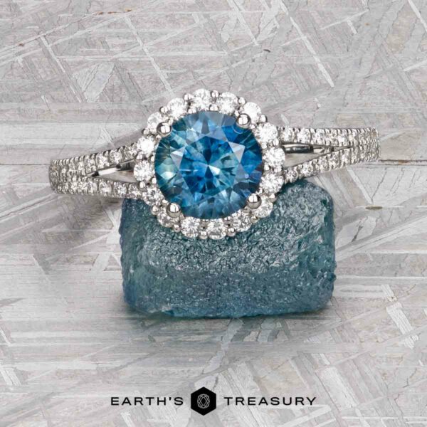 The "Charlotte" ring in 14K white gold with 1.71-carat Montana sapphire The "Charlotte" ring in 14K white gold features a 1.71-carat Montana sapphire, diamond halo, and diamond-accented band, shown on a rough blue crystal with the Earth’s Treasury logo below.