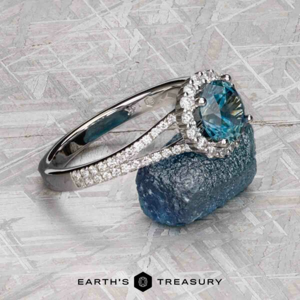 The "Charlotte" ring in 14K white gold with 1.71-carat Montana sapphire The "Charlotte" ring in 14K white gold features a 1.71-carat Montana sapphire in an oval halo setting, accented by diamonds and shown on a blue stone, with the Earth's Treasury logo below.