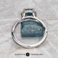 The "Charlotte" ring in 14K white gold with a 1.71-carat Montana sapphire is displayed upright against a rough blue mineral on a textured gray surface, with the Earth's Treasury logo at the bottom.