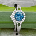 The "Charlotte" ring in 14K white gold with a 1.71-carat Montana sapphire, paired with the "Rhine" band in matching gold, is elegantly displayed on a green leaf.