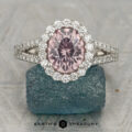 The "Charlotte" ring in platinum features a 1.67-carat round Mahenge garnet center stone, surrounded by clear accents, displayed on a textured blue stone base with the text "EARTH'S TREASURY" below.