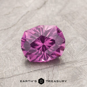 A faceted gemstone from product ET1127, featuring a pink hue, displayed on a textured gray surface.