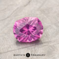 A faceted, round-cut magenta garnet gemstone (ET1127) rests on a textured gray surface with the text "EARTH'S TREASURY" and a simple logo below.