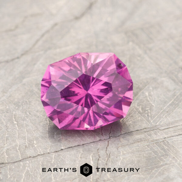 1.29-Carat Pastel Pyrope Color-Change Garnet A faceted, round-cut magenta garnet gemstone (ET1127) rests on a textured gray surface with the text "EARTH'S TREASURY" and a simple logo below.