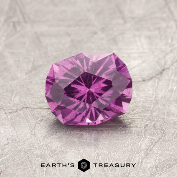 1.13-Carat Pastel Pyrope Color-Change Garnet A faceted pink gemstone, product ET1128, rests on a textured gray surface labeled "Earth's Treasury.