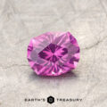 A faceted, oval-cut gemstone—ET1128, a Pyrope Garnet showcasing a striking magenta-purple color change—rests on a textured gray surface, with the "EARTH'S TREASURY" text and logo displayed below.
