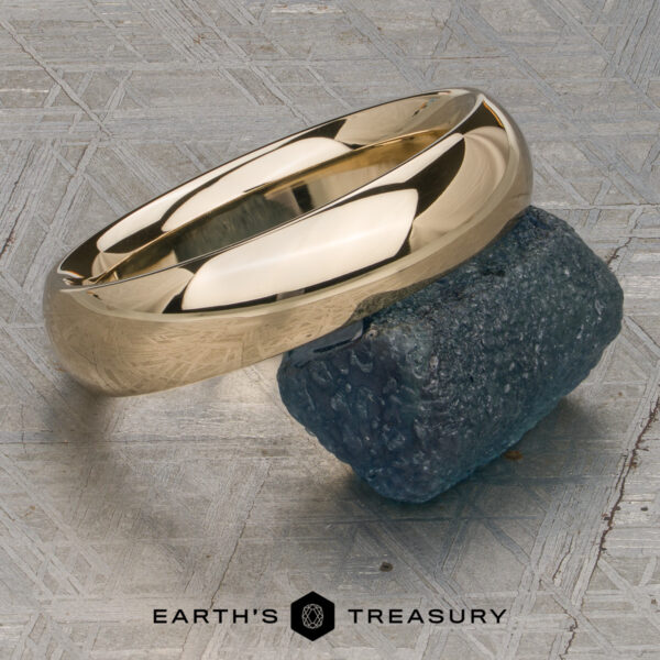 Classic Band, Comfort Fit in 14K yellow gold 5.0mm wide A Classic Band, Comfort Fit in 14K yellow gold (5.0mm wide), rests on a rough blue-green stone atop a textured gray surface with the "Earth's Treasury" logo below.