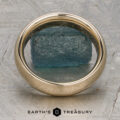 A Classic Band, Comfort Fit in 14K yellow gold (5.0mm wide), rests on a rough blue-green stone atop a textured gray surface with the "Earth's Treasury" logo below.