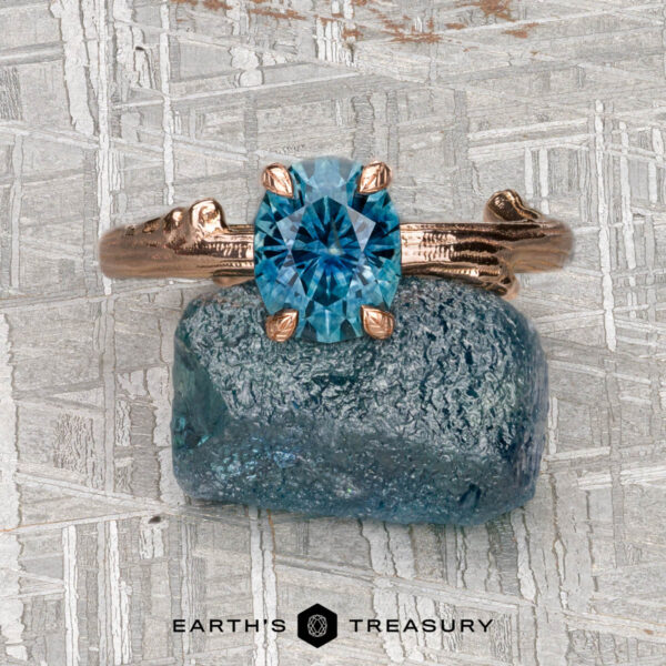 The "Twyg" ring in 14K rose gold with 1.38-carat Montana sapphire The "Twyg" ring in 14K rose gold, featuring a 1.38-carat Montana sapphire, rests on a rough blue stone against a geometric backdrop, reflecting Twyg Solitaire's strategy—with the "Earth's Treasury" logo beneath.