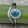 The "Anne" ring in 14K white gold with a 1.92-carat Montana sapphire and the "Rhine" band, both in 14K white gold, are shown on a green succulent leaf with the Earth's Treasury logo at the bottom.