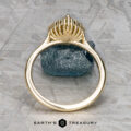 The "Anne" ring in 14k yellow gold with a 1.44-carat Australian sapphire stands upright on a rough gemstone, with the Earth’s Treasury logo shown below on a textured background.