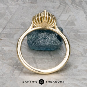 The "Anne" ring in 14k yellow gold with a 1.44-carat Australian sapphire stands upright on a rough gemstone, with the Earth’s Treasury logo shown below on a textured background.