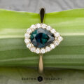 The "Anne" ring in 14k yellow gold features a 1.44-carat Australian sapphire, pear-shaped and surrounded by diamonds, displayed on a green leaf with "EARTH'S TREASURY" below.