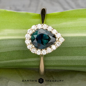 The "Anne" ring in 14k yellow gold features a 1.44-carat Australian sapphire, pear-shaped and surrounded by diamonds, displayed on a green leaf with "EARTH'S TREASURY" below.