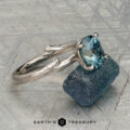 The "Twyg" ring in 14K white gold, featuring a 2.05-carat Montana sapphire, is displayed atop a rough blue stone with the text "Earth's Treasury" below.