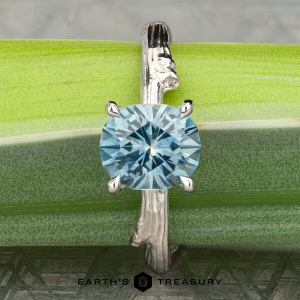 The "Twyg" ring in 14K white gold with 2.05-carat Montana sapphire The "Twyg" ring in 14K white gold with a 2.05-carat Montana sapphire is shown upright on a green Twyg bamboo stalk, with the Earth's Treasury logo at the bottom of the image.