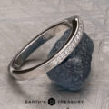 A platinum “Faye” band encircles a rough, dark green stone, displayed on a textured gray surface with the Earth’s Treasury logo at the bottom.