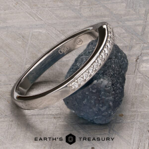 A platinum “Faye” band encircles a rough, dark green stone, displayed on a textured gray surface with the Earth’s Treasury logo at the bottom.