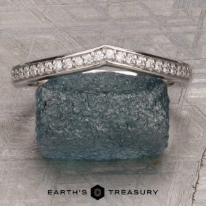 A platinum “Faye” band encircles a rough, dark green stone, displayed on a textured gray surface with the Earth’s Treasury logo at the bottom.