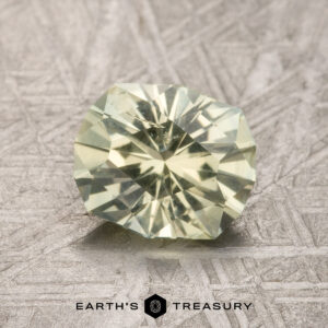 A 1.67-carat Light Yellow Montana Sapphire, round and faceted, is shown on a textured gray surface with the "Earth's Treasury" logo below.