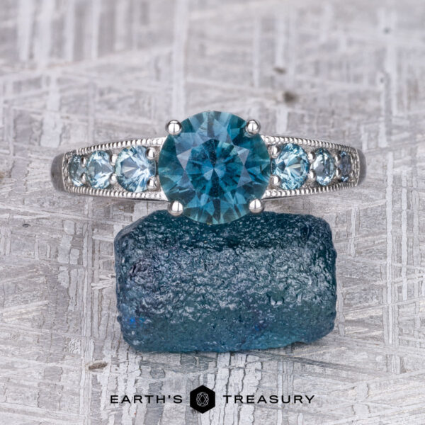 The "Cascade" ring in platinum with 2.05-carat Montana sapphire The "Cascade" ring in platinum features a 2.05-carat Montana sapphire, accented by smaller blue stones and set elegantly on a textured surface with blue crystal details.