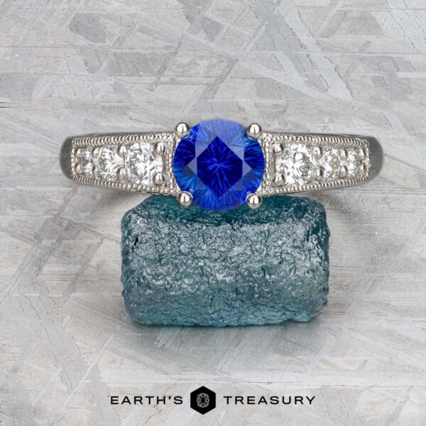 The "Cascade" ring in platinum with 1.24-carat Ceylon sapphire A platinum "Cascade" ring with a 1.24-carat Ceylon sapphire is showcased on rough blue crystal, with the "Earth's Treasury" logo beneath.