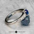 The "Cascade" ring showcases a platinum band with a 1.24-carat Ceylon sapphire, set elegantly on a textured grey surface.