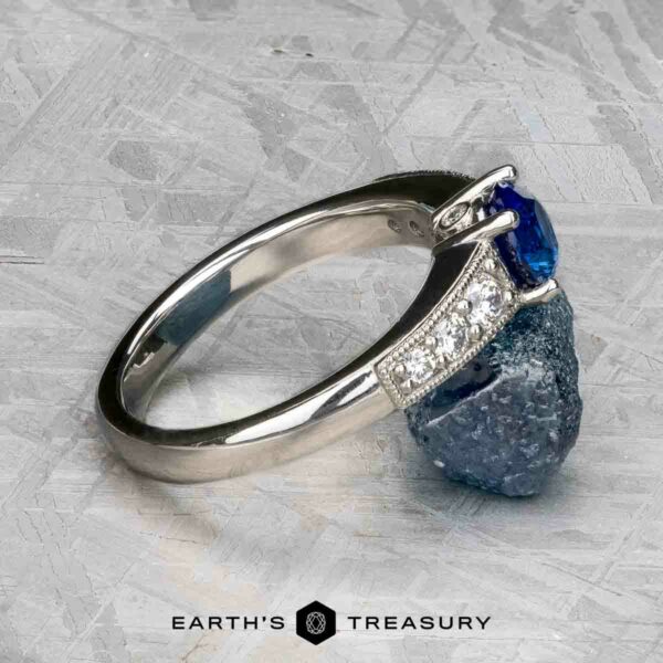 The "Cascade" ring in platinum with 1.24-carat Ceylon sapphire The "Cascade" ring showcases a platinum band with a 1.24-carat Ceylon sapphire, set elegantly on a textured grey surface.