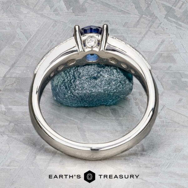The "Cascade" ring in platinum with 1.24-carat Ceylon sapphire The Cascade ring in platinum with a 1.24-carat Ceylon sapphire is displayed upright against a blue rock on textured gray, with the "Earth's Treasury" logo at the bottom.