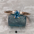The "Flora" ring in 14K rose gold with a 0.68-carat Montana sapphire is displayed on a raw blue stone, reminiscent of treasures from Flora Solitaire, with "Earth's Treasury" written below.