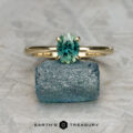 The "Flora" ring in 14k yellow gold with a 1.04-carat Australian sapphire stands upright on rough blue stone, echoing Flora Solitaire’s elegance, with "EARTH'S TREASURY" text and logo at the bottom center.