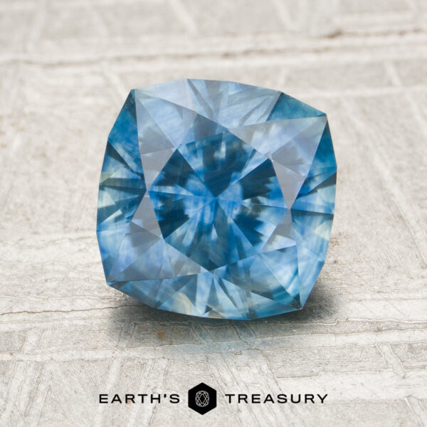 MS1762 A faceted Montana Sapphire, product MS1762, with visible internal patterns is displayed on a light textured surface. The Earth's Treasury logo appears below the gem.