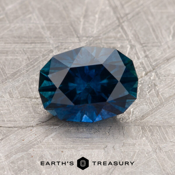 A 1.60-carat deep blue-green heated Montana sapphire is shown on textured gray, with "EARTH'S TREASURY" and a hexagon logo below.