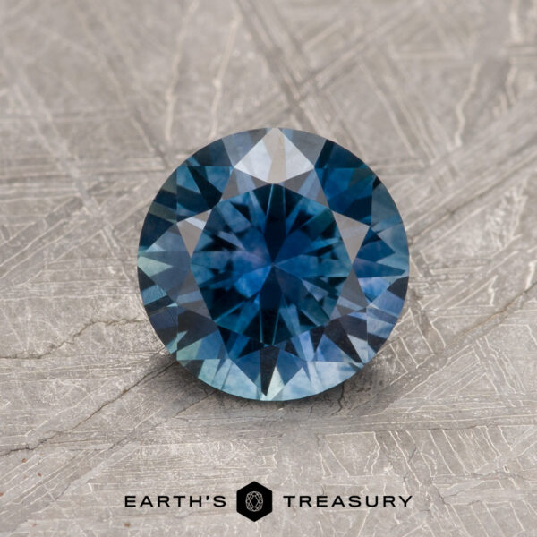 1.24-Carat Peacock Blue Montana Sapphire (Heated) A 1.24-Carat Peacock Blue Montana Sapphire (Heated) shines in vivid blue on a textured metallic background, with the text "Earth's Treasury" beneath.