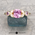 The "Calypso" ring in 14K yellow gold features a 1.24-carat Madagascar sapphire, accented by oval pink stones and marquise-shaped white stones, displayed on a rough blue crystal.