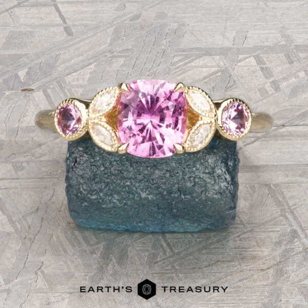 The "Calypso" ring in 14K yellow gold with 1.24-carat Madagascar sapphire The "Calypso" ring in 14K yellow gold features a 1.24-carat Madagascar sapphire, accented by oval pink stones and marquise-shaped white stones, displayed on a rough blue crystal.