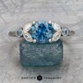 The "Calypso" ring in platinum features a 2.10-carat Montana sapphire as its centerpiece, flanked by two smaller gems and marquise-shaped accents—an elegant statement piece inspired by ocean hues.