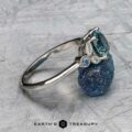 The "Calypso" ring in platinum with a 2.10-carat Montana sapphire is shown atop a rough blue mineral, with "Earth's Treasury" text below.