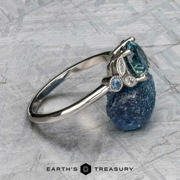 The "Calypso" ring in platinum with 2.10-carat Montana sapphire The "Calypso" ring in platinum with a 2.10-carat Montana sapphire is shown atop a rough blue mineral, with "Earth's Treasury" text below.