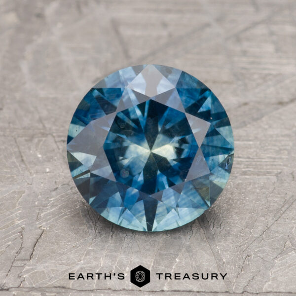 2.20-Carat Peacock Blue-Yellow Particolored Montana Sapphire (Heated) A 2.20-carat Peacock Blue-Yellow Particolored Heated Montana Sapphire is shown on a textured gray surface with the "Earth's Treasury" logo and text below it.