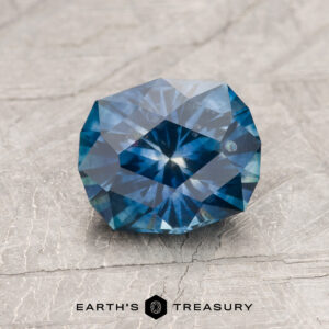A 1.79-carat rich blue heated Montana Sapphire gemstone, round and faceted, displayed on a light textured surface with the "Earth's Treasury" logo beneath.