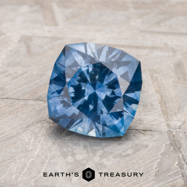 1.50-Carat Medium Blue Montana Sapphire (Heated) The faceted Medium Blue Montana Sapphire, product MS2237, rests on a textured light surface with "Earth's Treasury" and a hexagon logo shown below.
