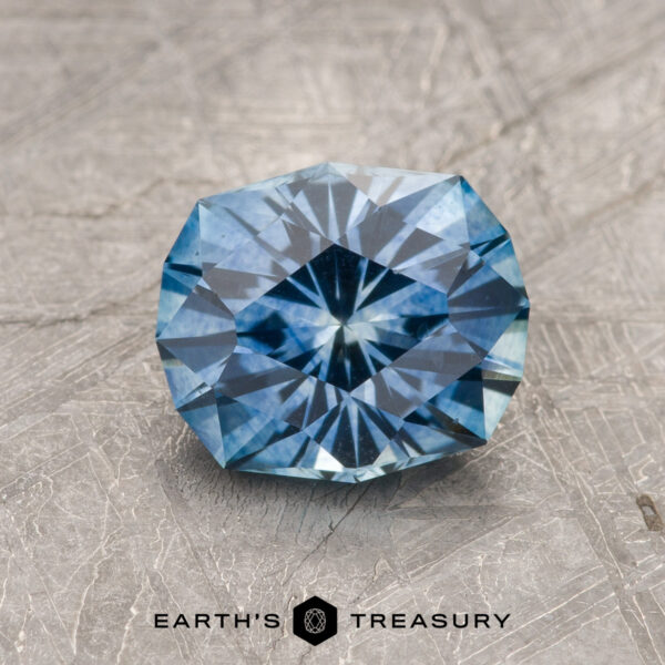 1.82-Carat Medium Blue Montana Sapphire (Heated) A 1.82-carat medium blue heated Montana Sapphire is showcased on a textured gray surface with "EARTH'S TREASURY" displayed at the bottom.