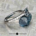 The "Meissa" ring in 14K white gold with a 1.47-carat Montana sapphire and diamond accents rests on a rough blue stone, its beauty enhanced by the metallic background and the Earth’s Treasury logo below.