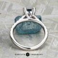 The "Meissa" ring in 14K white gold with a 1.47-carat rectangular Montana sapphire stands upright, a blue textured stone behind it and the Earth’s Treasury logo below.