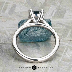 The "Meissa" ring in 14K white gold with a 1.47-carat rectangular Montana sapphire stands upright, a blue textured stone behind it and the Earth’s Treasury logo below.