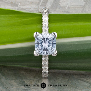 The "Meissa" ring in 14K white gold with a 1.47-carat Montana sapphire and diamond band rests on a green leaf, with the Earth's Treasury logo visible at the bottom of the image.